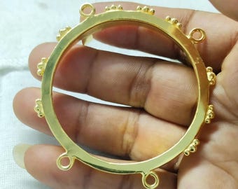 Könnte beinhalten: Ein goldfarbenes, kreisförmiges Schmuckelement mit dekorativen floralen und perlenartigen Akzenten. Das Element hat mehrere Schlaufen zur Befestigung und wird in einer Hand gehalten.