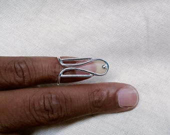 May include: A silver-colored finger ring with a unique, open design. The ring wraps around the finger, featuring a curved top and a lower loop. The ring is shown on a finger against a neutral background.