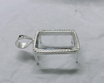 Puede incluir: Un colgante plateado con un marco rectangular y un borde decorativo en forma de cuerda. El colgante tiene un pequeño lazo para una cadena y cuatro patas pequeñas. Diseñado para sostener una piedra u otro inserto.