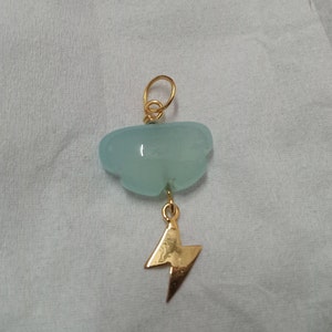 May include: A gold pendant with a light blue gemstone shaped like a cloud and a gold lightning bolt charm.