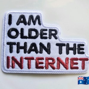 May include: A white embroidered patch with a stepped edge featuring the black text I AM OLDER THAN THE and the red text INTERNET. The patch has a white border and a white fabric background with a diagonal weave texture throughout the design.
