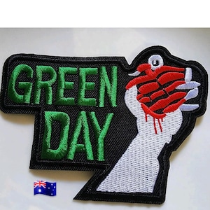 Può includere: Toppa ricamata con la scritta "GREEN DAY" in verde su sfondo nero. Il disegno include un pugno bianco con artigli rossi e sangue che cola. È presente anche una piccola bandiera australiana.