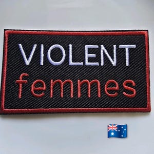 May include: A rectangular embroidered patch with a black background and a red border. The text VIOLENT is stitched in white capital letters, and the text femmes is stitched below in red lowercase letters. A small Australian flag icon is visible.