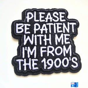 May include: A black embroidered patch with a scalloped edge featuring white stitched text that reads: PLEASE BE PATIENT WITH ME I'M FROM THE 1900'S. The patch has a textured fabric surface and is displayed alongside a small Australian flag icon.
