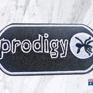 May include: An oval-shaped embroidered patch with a black background and a white border. The text "prodigy" is stitched in white letters on the left side, and a white circular icon featuring a black ant graphic is positioned on the right side.