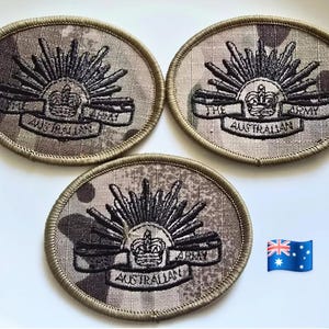 May include: Three oval-shaped embroidered patches with a camouflage pattern. Each patch features a sunburst design with a crown and banner that reads "THE AUSTRALIAN ARMY". The patches are surrounded by a beige border.