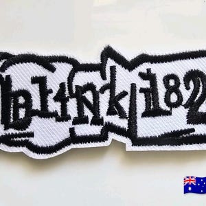 Könnte beinhalten: Ein rechteckiger gestickter Aufnäher mit dem Text blink-182 in einer stilisierten schwarzen gotischen Schriftart. Die Schrift befindet sich auf einem weißen Hintergrund mit einem dicken, schwarz gestickten Rand, der der Kontur folgt.