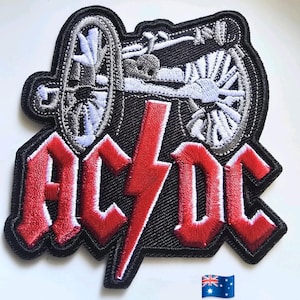 May include: Embroidered patch with the band name "AC/DC" in red gothic lettering and a red lightning bolt. The design includes a detailed illustration of a cannon in grey and white against a black background. The Australian flag is in the bottom right corner.