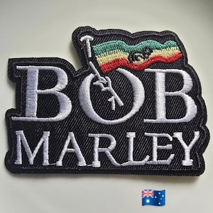 Peut inclure: Écusson brodé noir avec le nom "BOB MARLEY" en lettres blanches. Un drapeau aux rayures vertes, jaunes et rouges est représenté au-dessus du nom. L'écusson a une bordure noire.