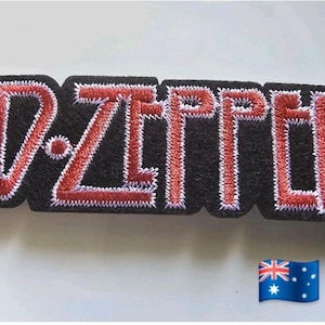 Puede incluir: Parche bordado con el nombre de la banda "LED ZEPPELIN" en hilo rojo sobre fondo negro. El parche tiene un borde cosido blanco. Una bandera australiana está en la esquina inferior derecha.