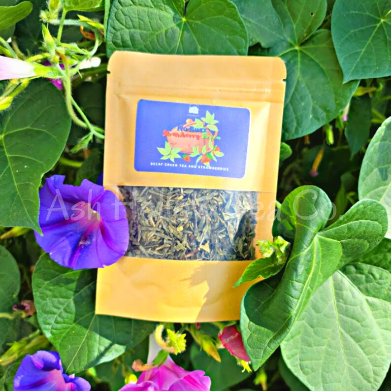 May include: A small, yellow pouch with a clear window showing loose green tea leaves. The pouch has a label that reads "No Buzz Strawberry Bliss" and "Decaf Green Tea and Strawberries".
