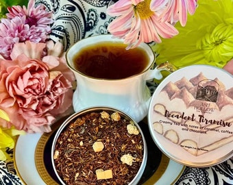 May include: A round tin of loose leaf tea with a label that reads "Decadent Tiramisu" and "Creamy Tea with notes of caramel, coffee, and chocolate." The tin is open and the tea is visible. The tea is a blend of red and brown tea leaves with small white pieces.