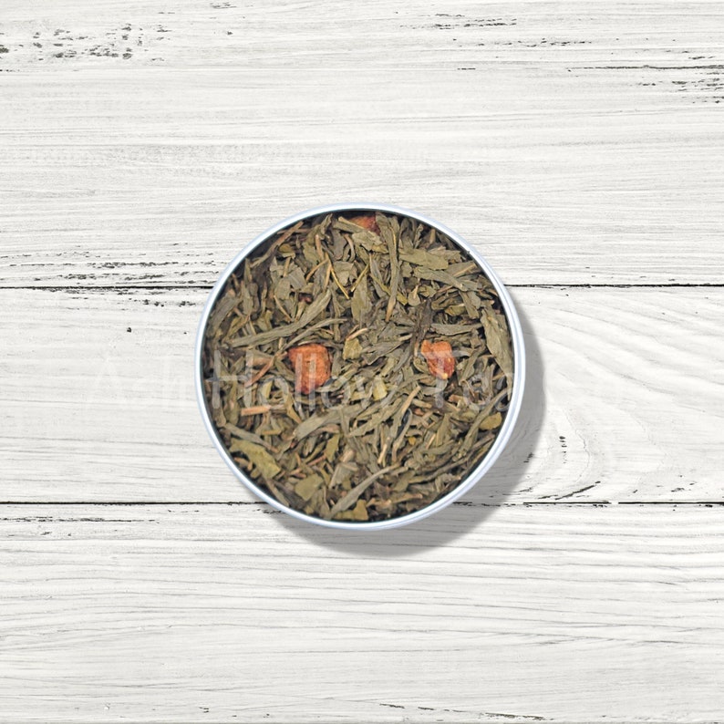 May include: A round metal tin filled with loose leaf green tea and dried fruit pieces. The tea is a mix of green leaves and small pieces of dried fruit.