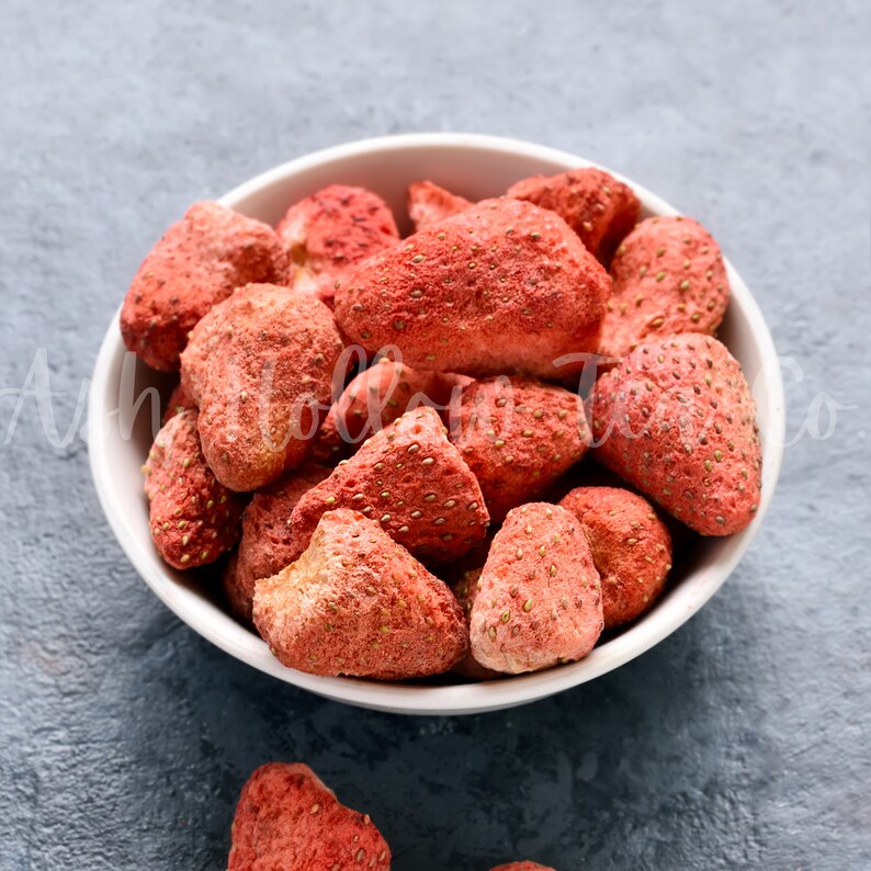 May include: A white bowl filled with freeze-dried strawberries. The strawberries are a vibrant red color and have a slightly textured surface.