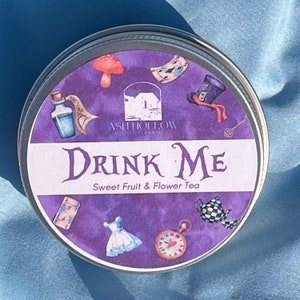 May include: A purple and white tin with the words "Drink Me" and "Sweet Fruit & Flower Tea" printed on it. The tin is decorated with images from Alice in Wonderland, including a mushroom, a playing card, a Mad Hatter's hat, a bottle, a pocket watch, a teacup, and a dress.