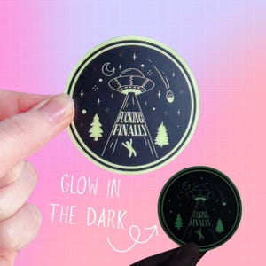 May include: Round black sticker with a neon green border and a glow-in-the-dark design. The design features a UFO beaming down on a stick figure, with the text "Fucking Finally". Includes trees, stars, and a crescent moon.