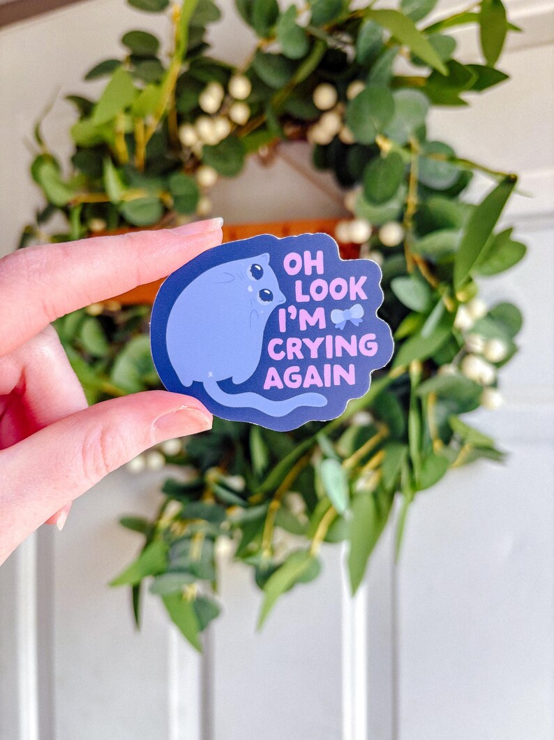 May include: A blue cat sticker with the text 'Oh look I'm crying again' in pink and white text.