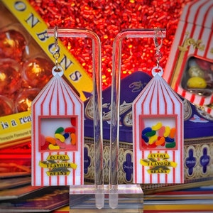 May include: A pair of red and white striped earrings with a clear window showing colorful jelly beans. The earrings have a yellow banner that reads "Every Flavour Beans".