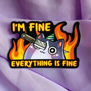 Könnte beinhalten: Ein Aufkleber mit einer Cartoon-Katze mit einem Messer im Auge, vor einem Hintergrund aus Flammen. Der Text "I'm fine" befindet sich über der Katze und "Everything is fine" unter der Katze.