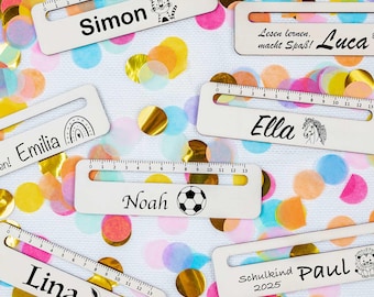 May include: A set of six white wooden rulers with colourful confetti in the background. Each ruler has a different name and a small illustration. The names are Simon, Luca, Emilia, Noah, Lina, and Paul.