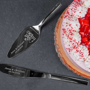 Könnte beinhalten: Ein Edelstahl-Kuchenservierer und Messerset mit eingravierten Namen und Datum, neben einem Erdbeerkuchen mit Schlagsahne. Der Servierer zeigt ein Brautpaar-Design. Der Kuchen steht auf einem Holzsockel.