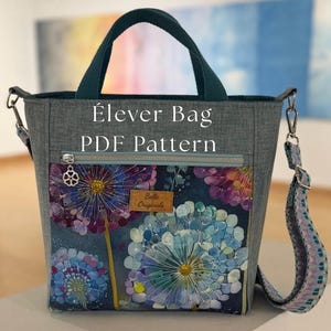 May include: Grey Élever Bag PDF Pattern with a floral design on the front pocket. The bag has a teal handle and a detachable shoulder strap with a patterned design. The text "Élever Bag PDF Pattern" is printed on the bag.