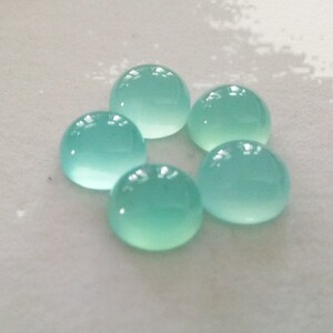 May include: Five round, cabochon-cut, light blue gemstones. The gemstones are smooth and polished.