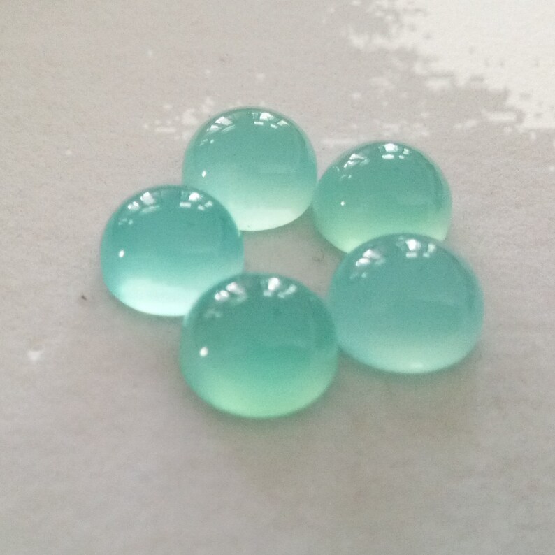 May include: Five round, cabochon-cut, light blue gemstones. The gemstones are smooth and polished.