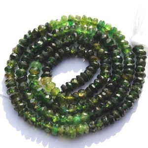Può includere: Un filo di perline di tormalina verde sfaccettate. Le perline variano nelle tonalità di verde, dal verde foresta intenso a tonalità verde-giallastre più chiare. Le perline sono infilate, con un nappa bianca all'estremità.