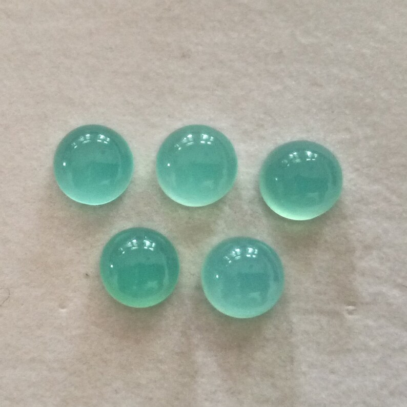 May include: Six round, smooth, turquoise cabochon gemstones on a white surface.