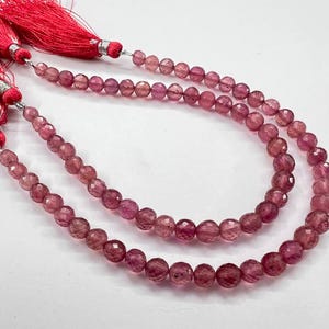 May include: A strand of pink gemstone beads with faceted surfaces. The beads are strung on a cord and have a tassel on each end.