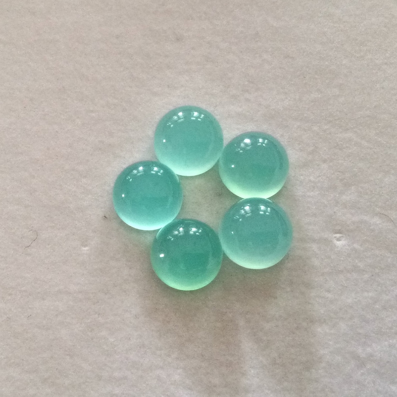 May include: Six round, smooth, light blue cabochon gemstones on a white surface.