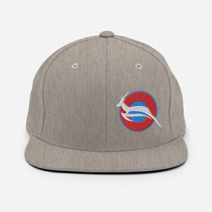 May include: A light gray baseball cap with a flat brim. The cap features an embroidered emblem of a white antelope leaping within a red and blue circular design. The cap is made of a textured fabric and has a button on top.