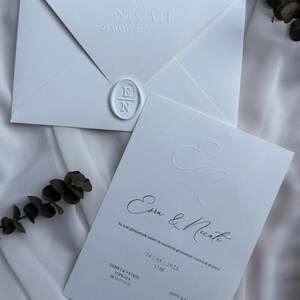 May include: Elegant white wedding invitation suite with embossed details and a wax seal. The invitation features the names "Esra & Necati" and the date "24 MAYIS 2025". The suite includes an envelope and a card with further information.