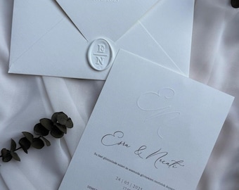 May include: White wedding invitation suite featuring embossed text and a wax seal. The invitation includes the names "Esra & Necati" and the date "24 MAYIS 2025". The suite includes an envelope and a card with additional details.