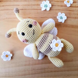 Handmade organic cotton bee plush in vanilla tones sitting in a woven basket, sustainable artisan baby gift.