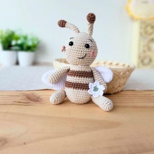 Beige edition handmade bee plush sitting on a wooden surface, natural cotton nursery toy.