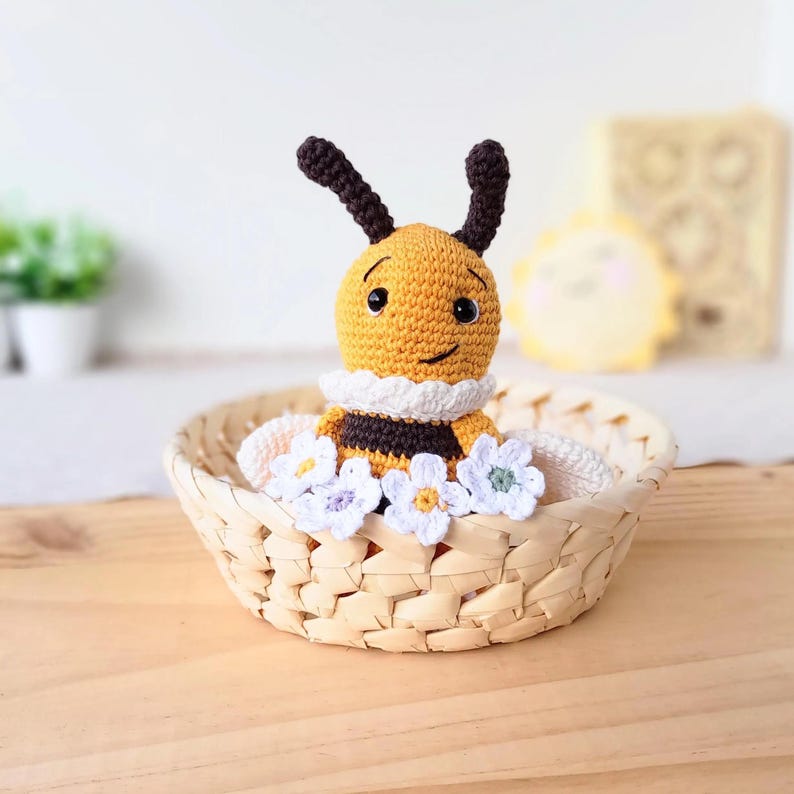 Yellow edition organic cotton bee plush sitting in a small basket, artisan newborn keepsake.