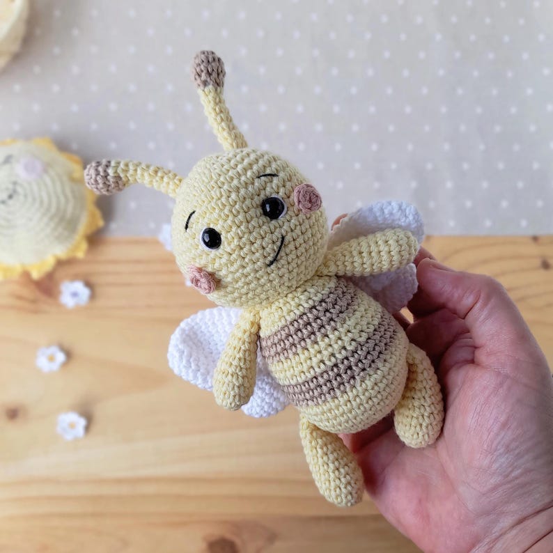 Organic cotton bee plush held in an adult hand, showing soft crochet texture for newborn gift.