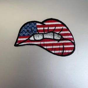 May include: Embroidered iron-on patch of a red, white, and blue American flag in the shape of a pair of lips.
