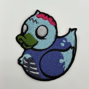 May include: A blue and purple embroidered patch of a zombie rubber duck with green eyes and a pink brain.