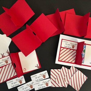 Peut inclure: Ensemble de cartes et &eacute;tiquettes de No&euml;l rouges et blanches. Les cartes pr&eacute;sentent un motif &agrave; rayures rouges et blanches et le texte "It's Christmas, let your light shine". Certaines cartes sont pli&eacute;es, r&eacute;v&eacute;lant des int&eacute;rieurs vierges. Th&egrave;me de vacances festives.