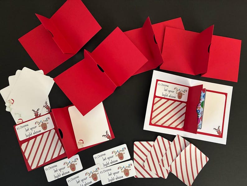 Peut inclure: Ensemble de cartes et &eacute;tiquettes de No&euml;l rouges et blanches. Les cartes pr&eacute;sentent un motif &agrave; rayures rouges et blanches et le texte "It's Christmas, let your light shine". Certaines cartes sont pli&eacute;es, r&eacute;v&eacute;lant des int&eacute;rieurs vierges. Th&egrave;me de vacances festives.