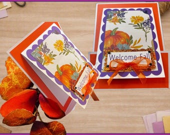 May include: A DIY card kit featuring two greeting cards with orange and white cardstock, scalloped purple borders, and a floral pumpkin print. Each card displays a rectangular label with the text Welcome Fall and an orange organza ribbon bow.