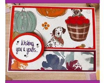 May include: A rectangular greeting card featuring a pattern of pumpkins, a basket of red apples, and dogs, including a dalmatian and a pug. A circular red-bordered tag is attached to the front with the text Wishing you & yours... in purple.