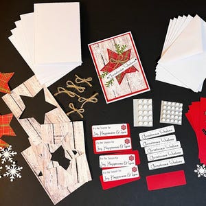 Peut inclure: Un ensemble de fournitures de bricolage sur le th&egrave;me de No&euml;l, comprenant des cartes vierges, des enveloppes, des d&eacute;coupes en forme d'&eacute;toile et des &eacute;l&eacute;ments d&eacute;coratifs. La palette de couleurs comprend des tons rouges, blancs et bruns, avec des accents de vert et d'or. Le texte "Christmas Wishes".