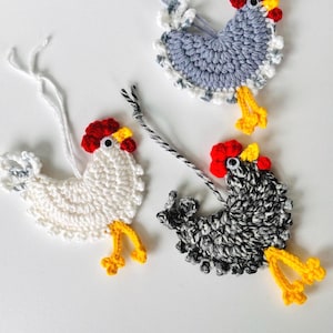 May include: Three crocheted chicken ornaments, one white, one gray, and one black and white. Each chicken has a red comb, yellow beak, and yellow feet.