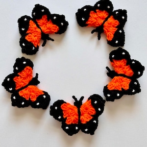 May include: Five crocheted orange and black butterflies with white bead accents arranged in a circle on a white background.