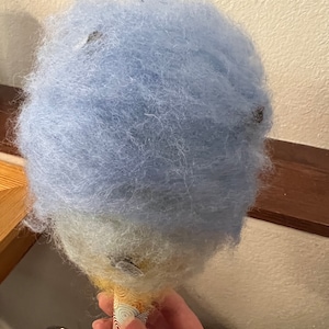 May include: A blue and white cotton candy cone. The cotton candy is fluffy and light blue on top, fading to white at the bottom.