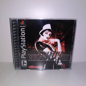 May include: A PlayStation game case with a black background and a woman in a white hat and black dress. The game title is "The Getaway" in red and black text.